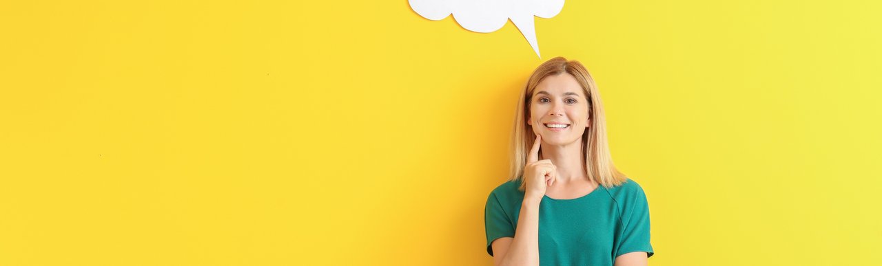 Eine Frau steht vor einer gelben Wand und lächelt. Über ihrem Kopf befindet sich eine weiße Sprechblase. Sie trägt ein türkisfarbenes Kleid und hält nachdenklich eine Hand ans Kinn.